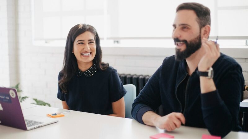 two people team laptop smiling laughing happy pen office