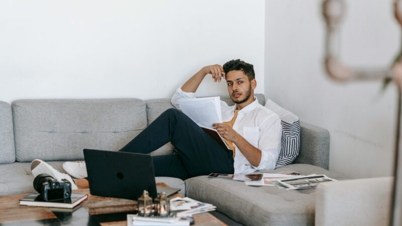 person sitting on sofa reading paperwork with laptop