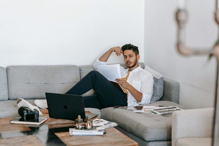 person sitting on sofa reading paperwork with laptop